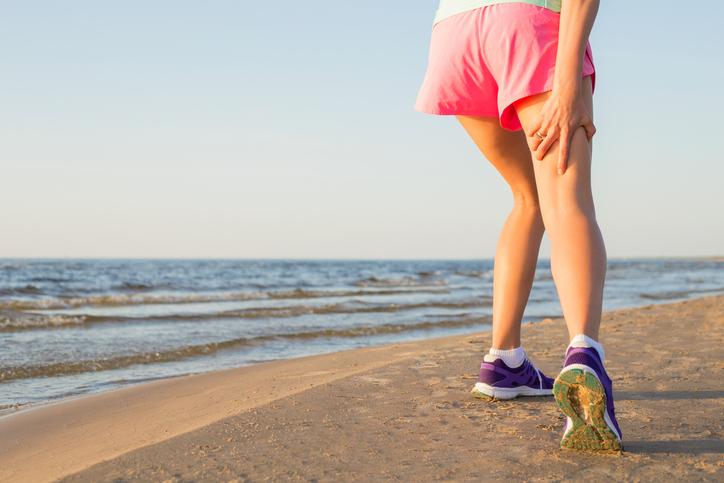 Running girl injured hamstring on beach Running girl injured hamstring on beach